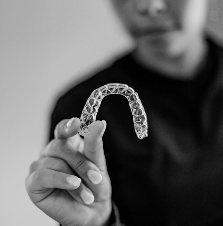 Woman holding a clear plastic retainer in front of a black shirt.